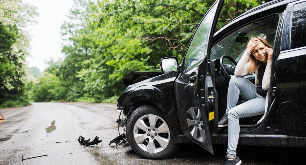Nach einem Mietwagen-Unfall sitzt eine verzweifelte Frau in einem beschädigten Wagen und telefoniert.